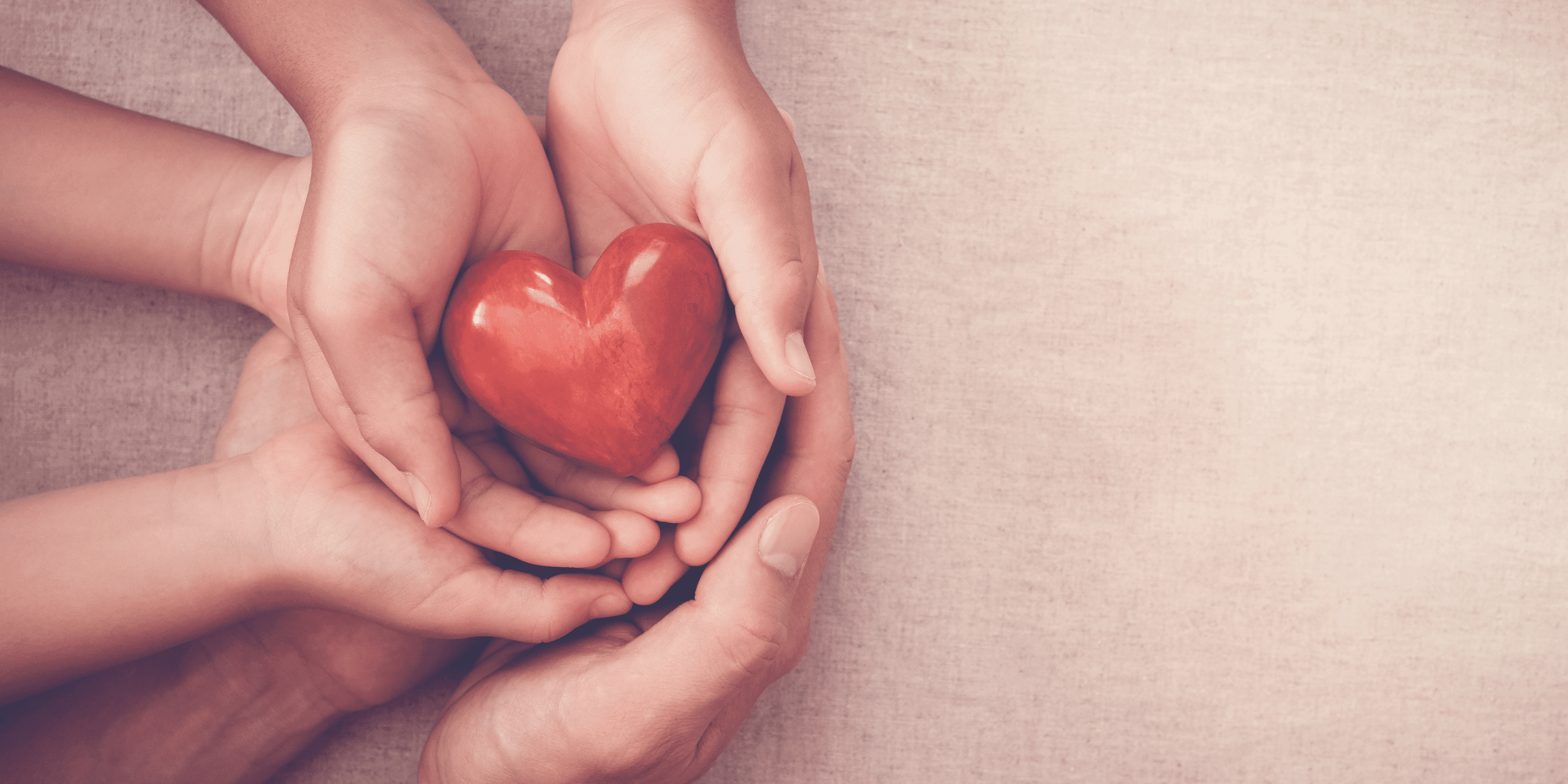 Adult hands hold child hands which hold a heart 