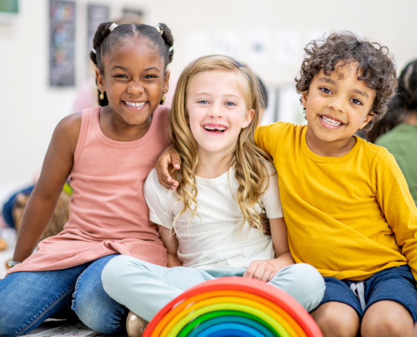 Three young children smiling in classroom setting