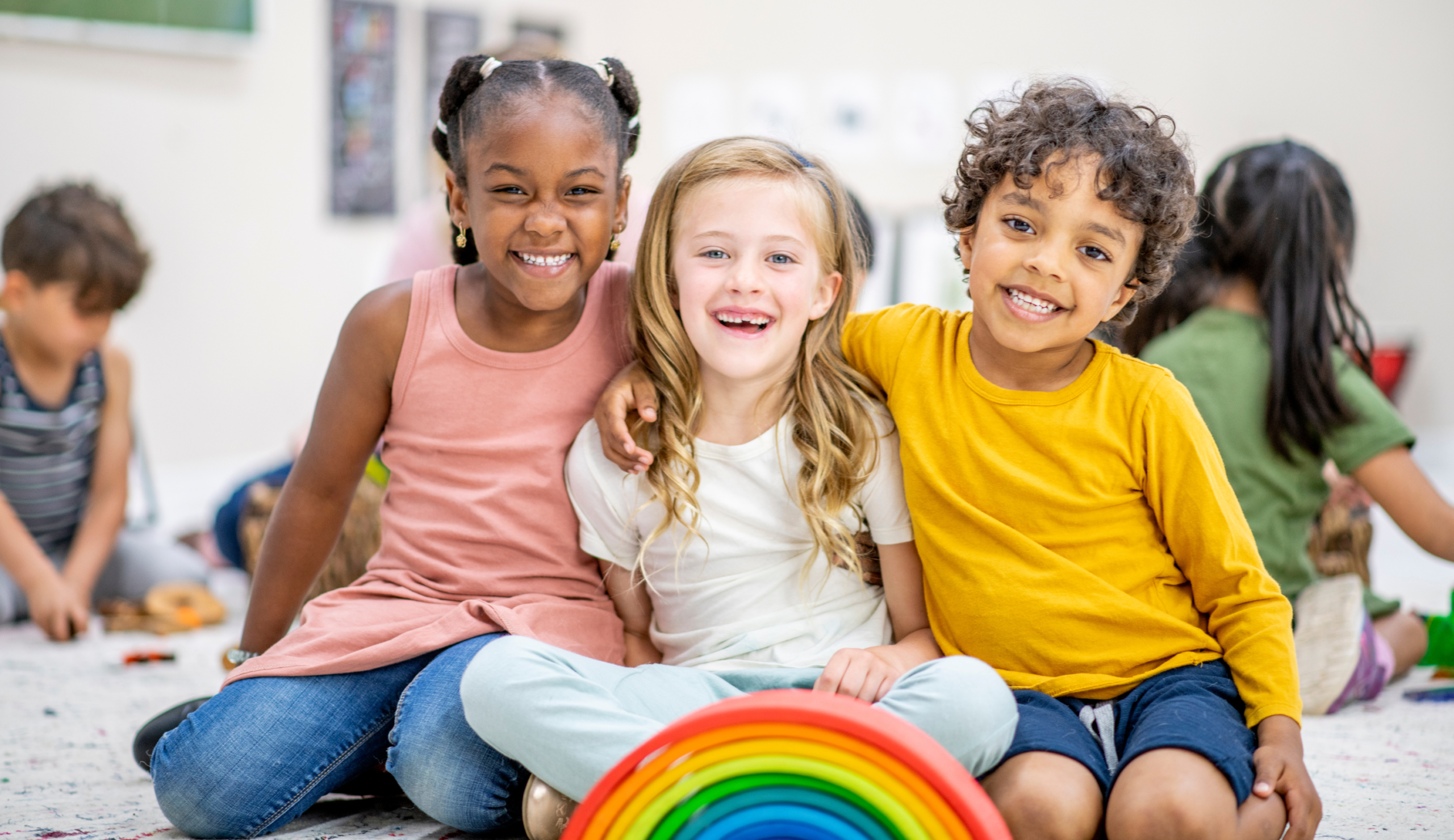 Three young children smiling in classroom setting 