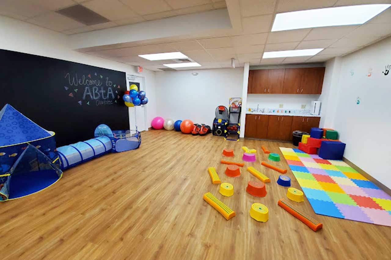 ABtA's gym set up with colorful floor pads, balls, and a chalkboard wall