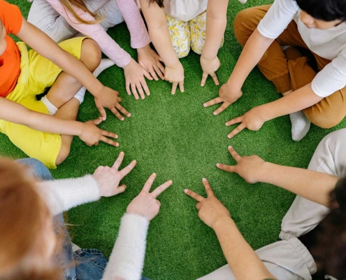 A circle of children's hands holding up two fingers pressed on a rug