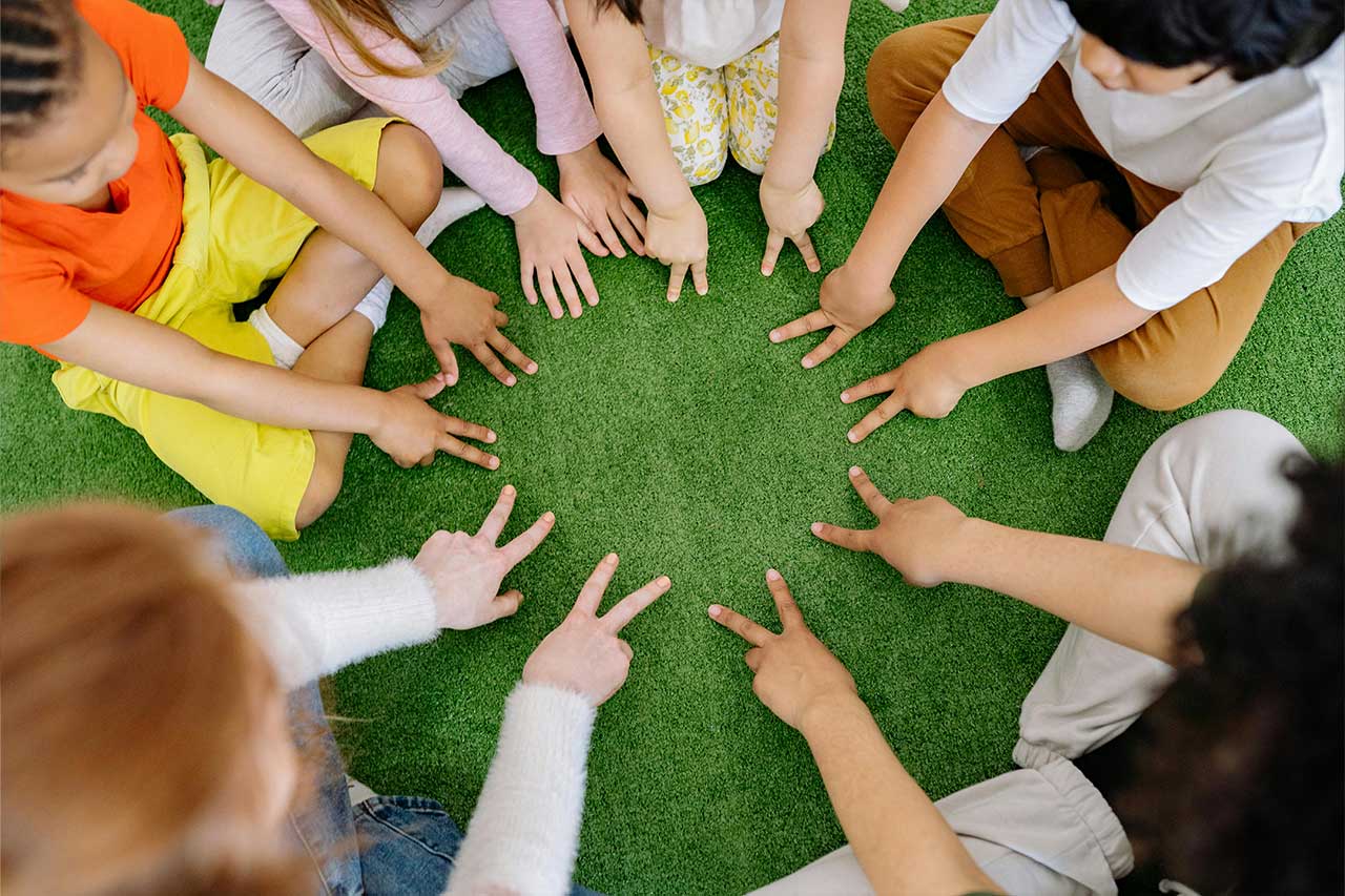 A circle of children's hands holding up two fingers pressed on a rug