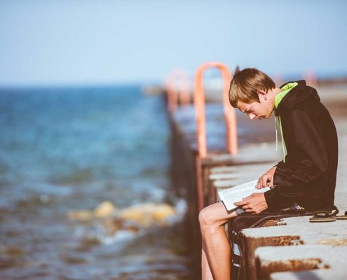 boy sitting at the ocean and reading a book