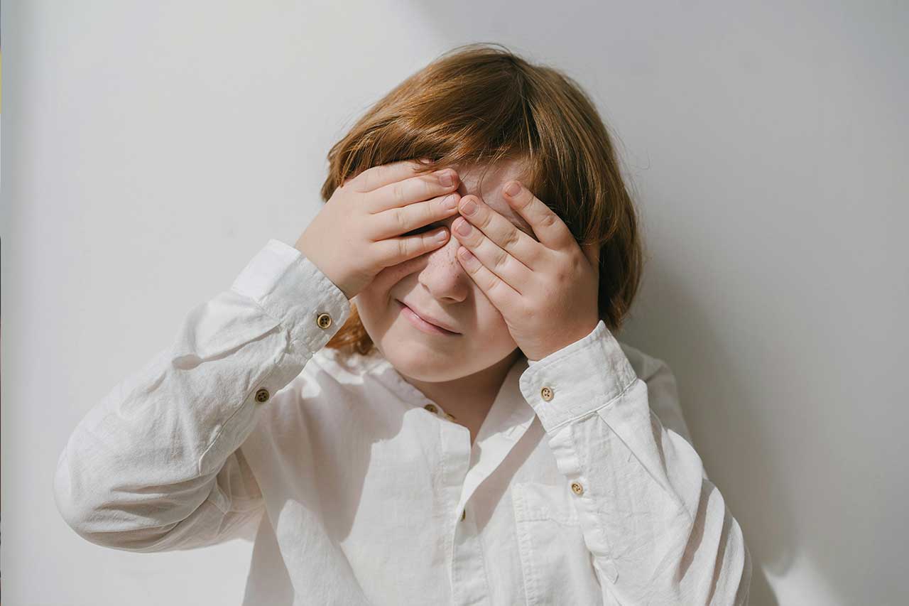 A child with their hands over their eyes peeking through their fingers.