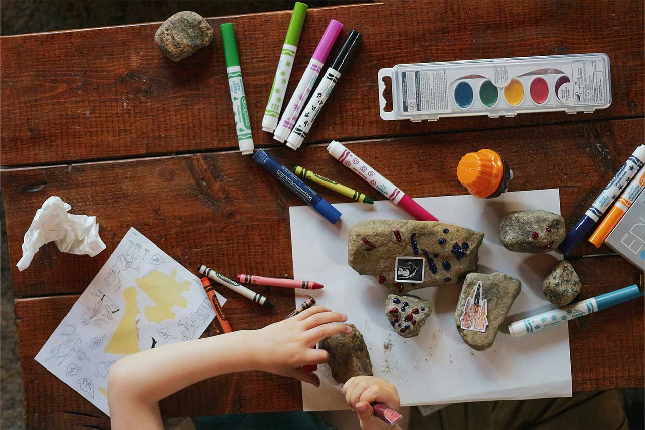 Child uses markers and paints to decorate rocks