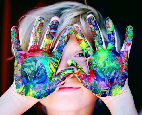 child with colorful paint on their hands and holding them in front of their face