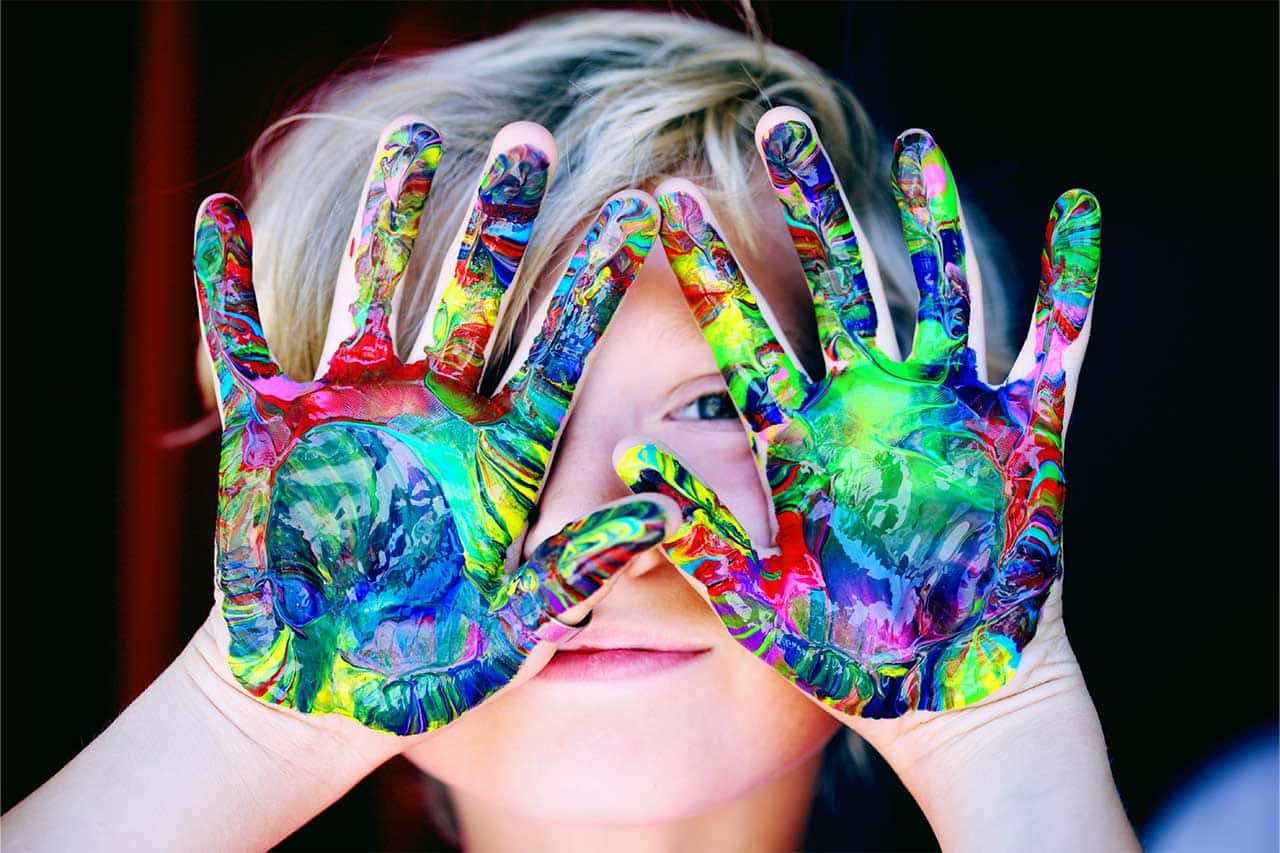 child with colorful paint on their hands and holding them in front of their face